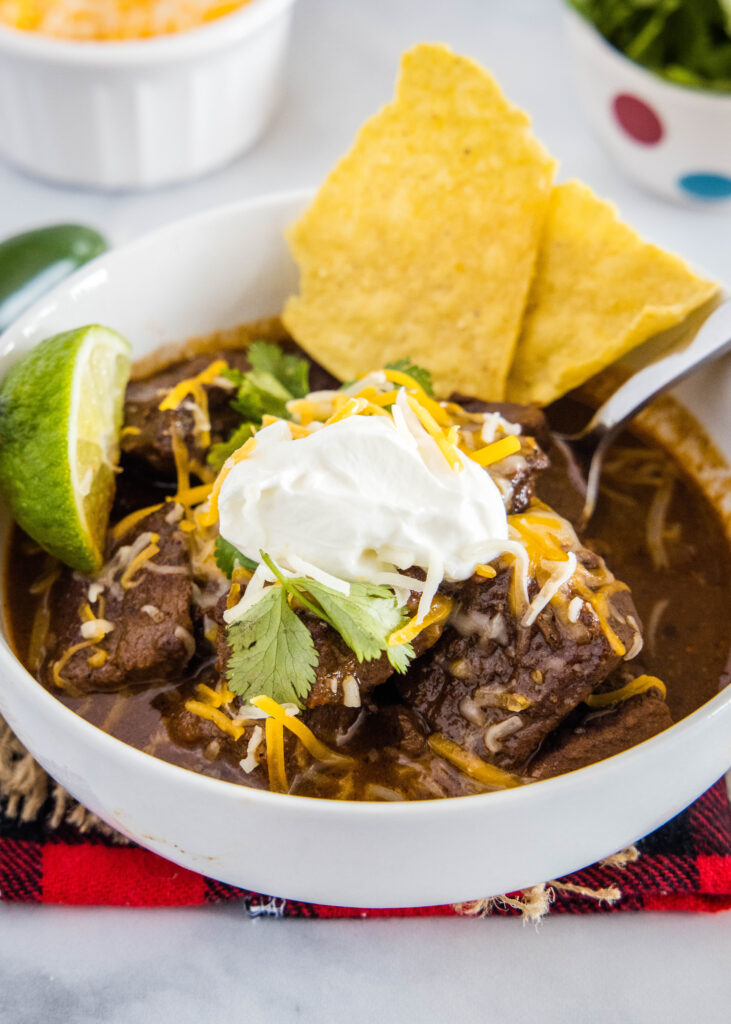 texas beef chili in a bowl topped with sour cream, cheese and tortilla chips