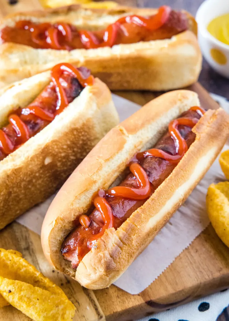 hot dogs topped with ketchup in a bun on a cutting board