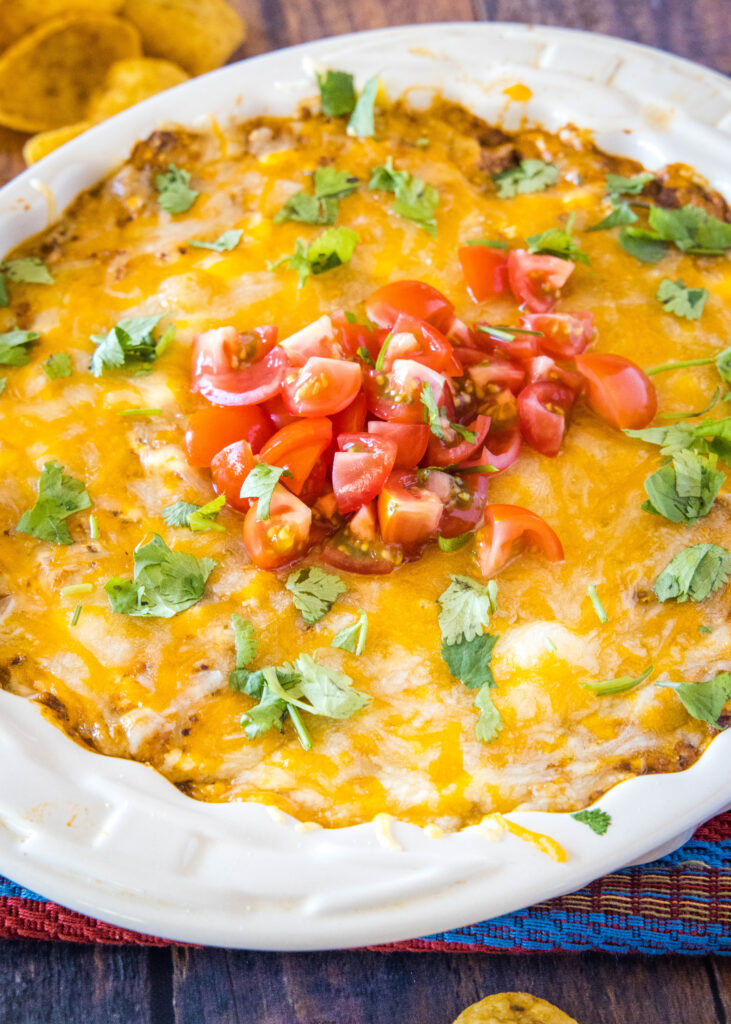 chili cheese dip in a dish topped with fresh tomatoes