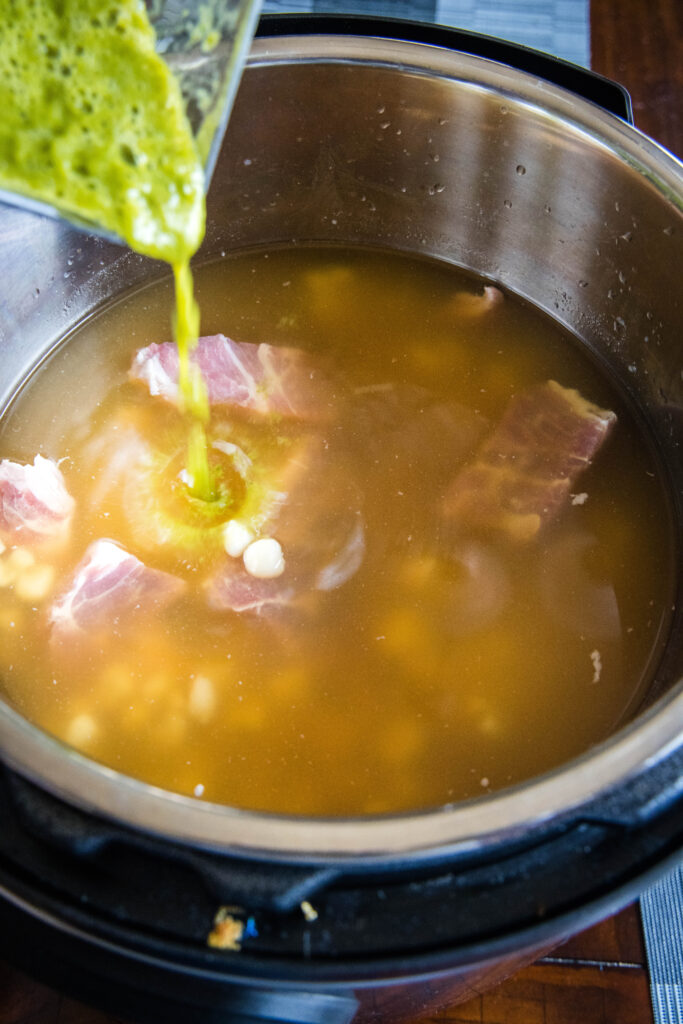 pouring salsa verde into instant pot with pork and hominy