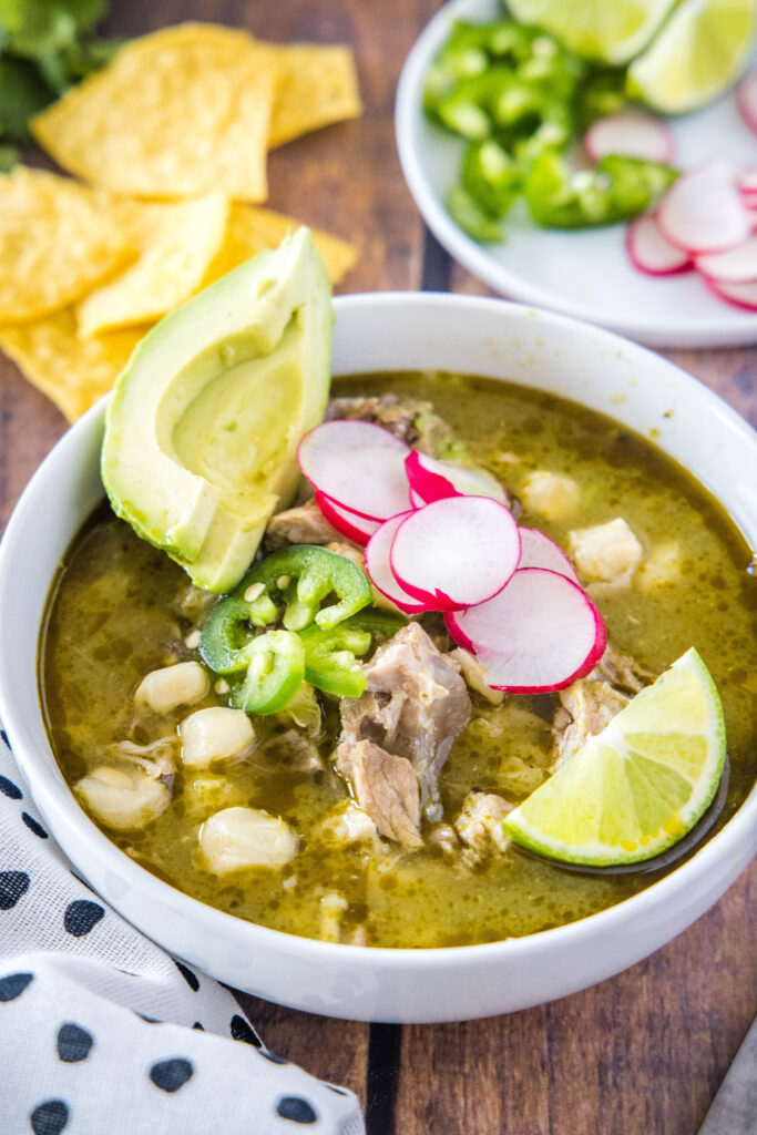 bowl of pozole topped with radishes, avocado and lime