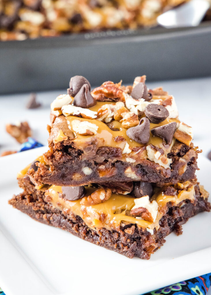 brownies with pecans, caramel and chocolate stacked on a plate