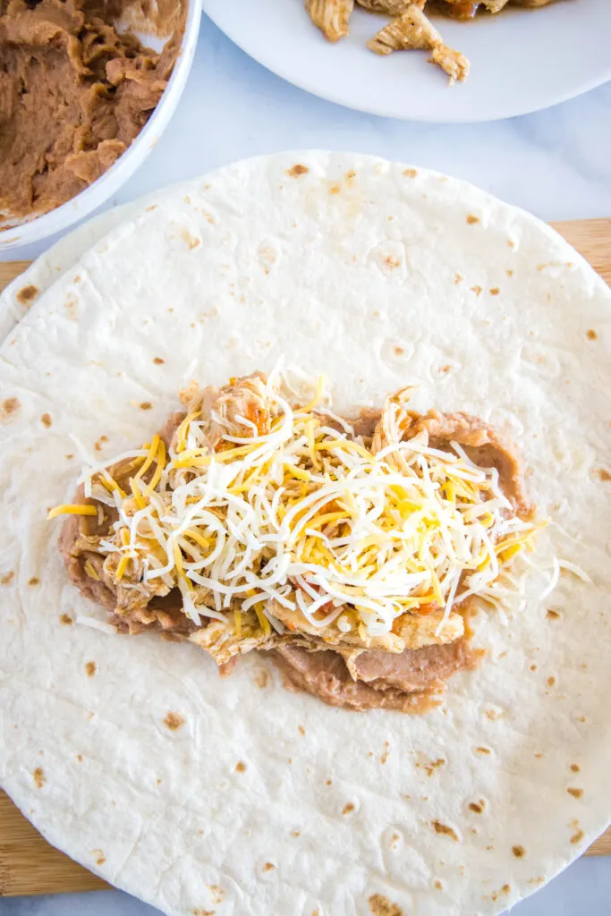 filling a tortilla with beans, chicken and cheese