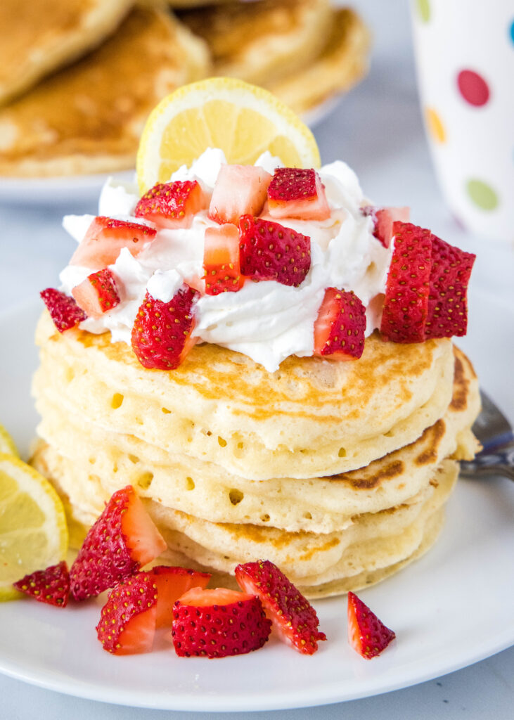stack of pancakes with whipped cream, strawberries and lemon
