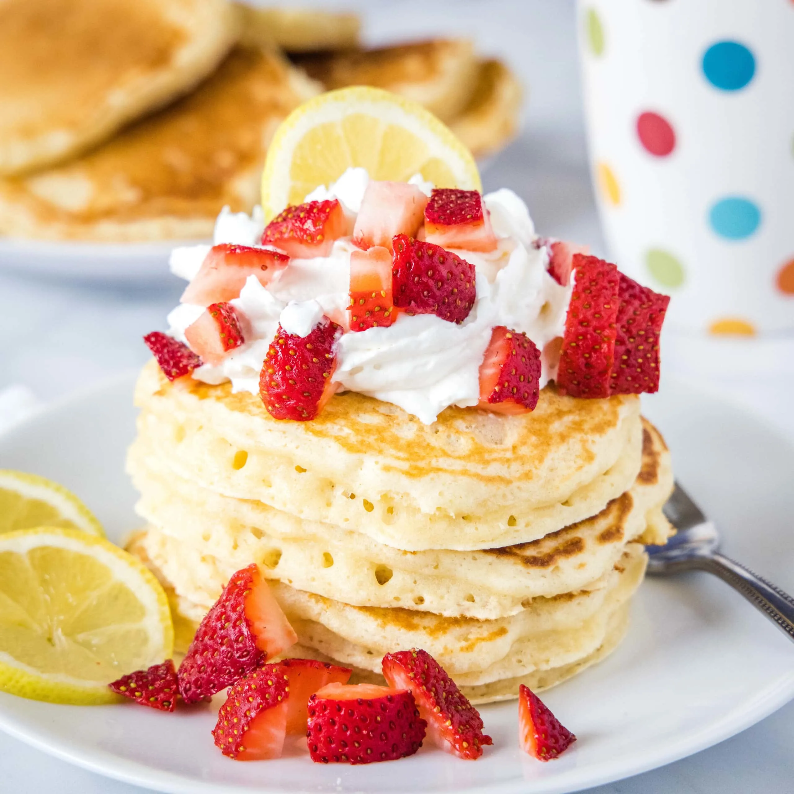 stack of lemon pancakes on white plate with strawberries