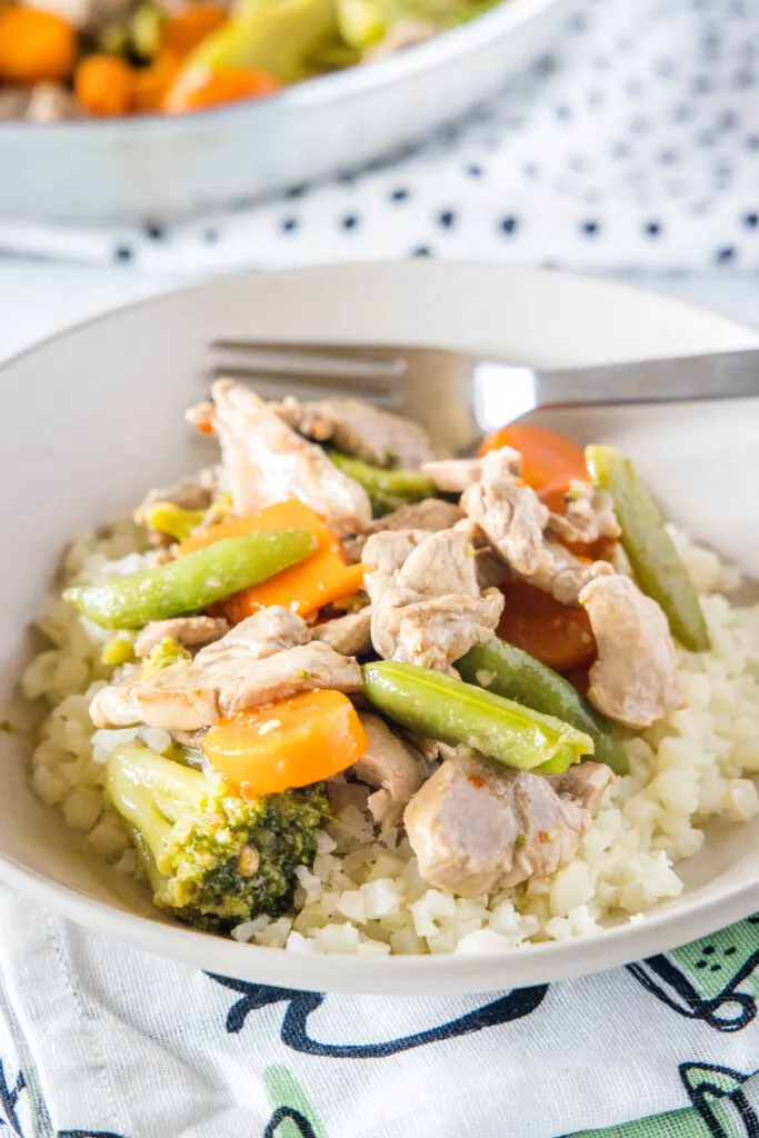 pork stir fry served over rice in a white bowl