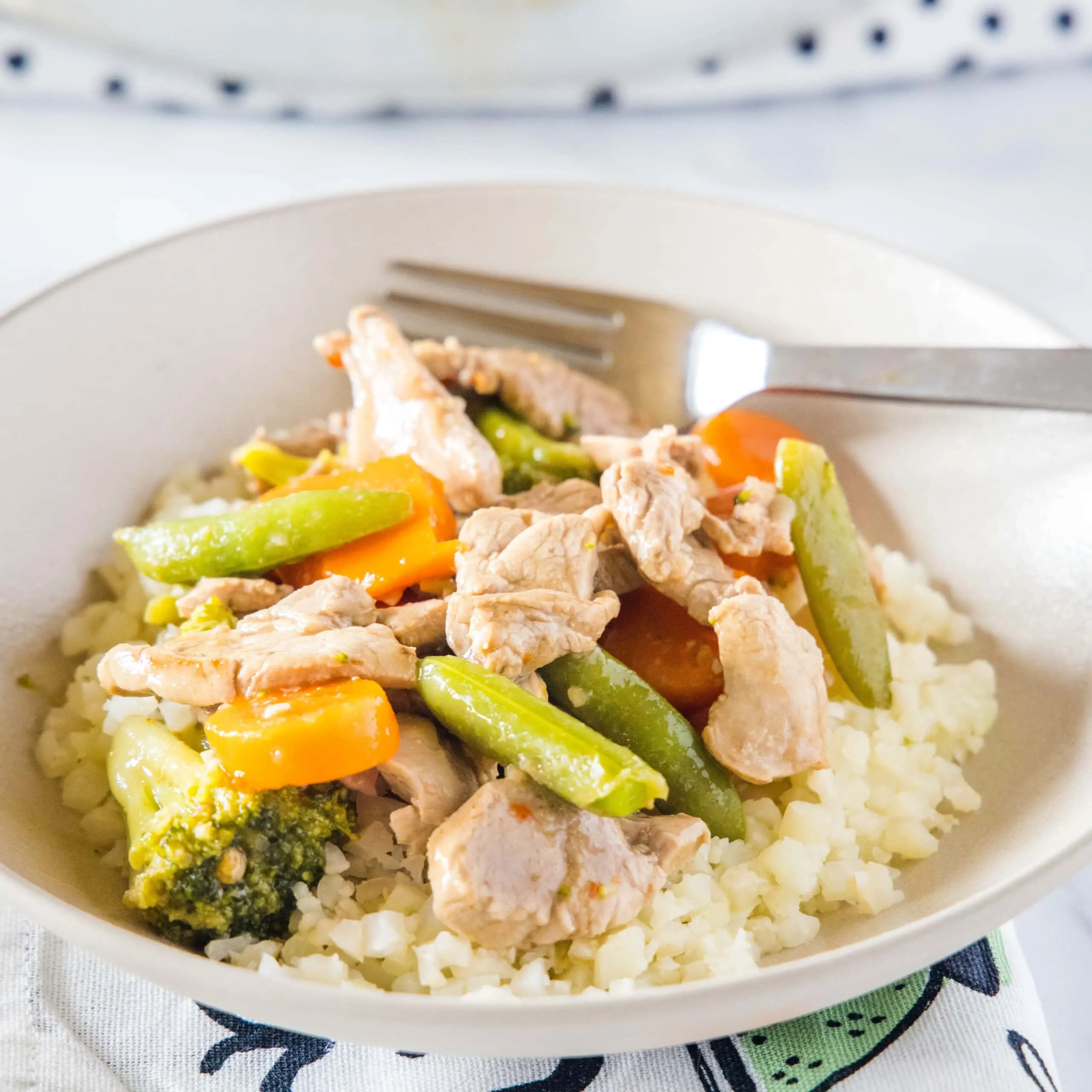 cropped close up of pork stir fry with veggies in a white bowl with rice