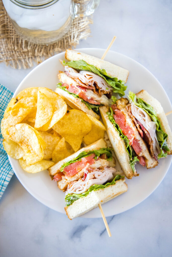 turkey club sandwich on a white plate with potato chips