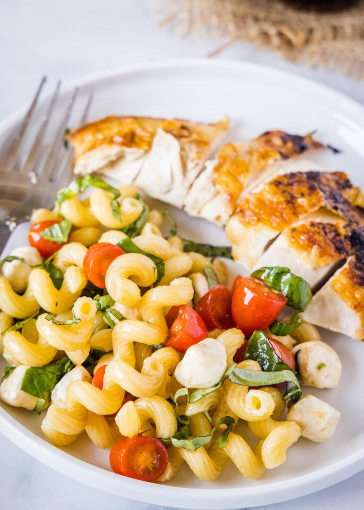 caprese pasta salad on a plate with a piece of chicken
