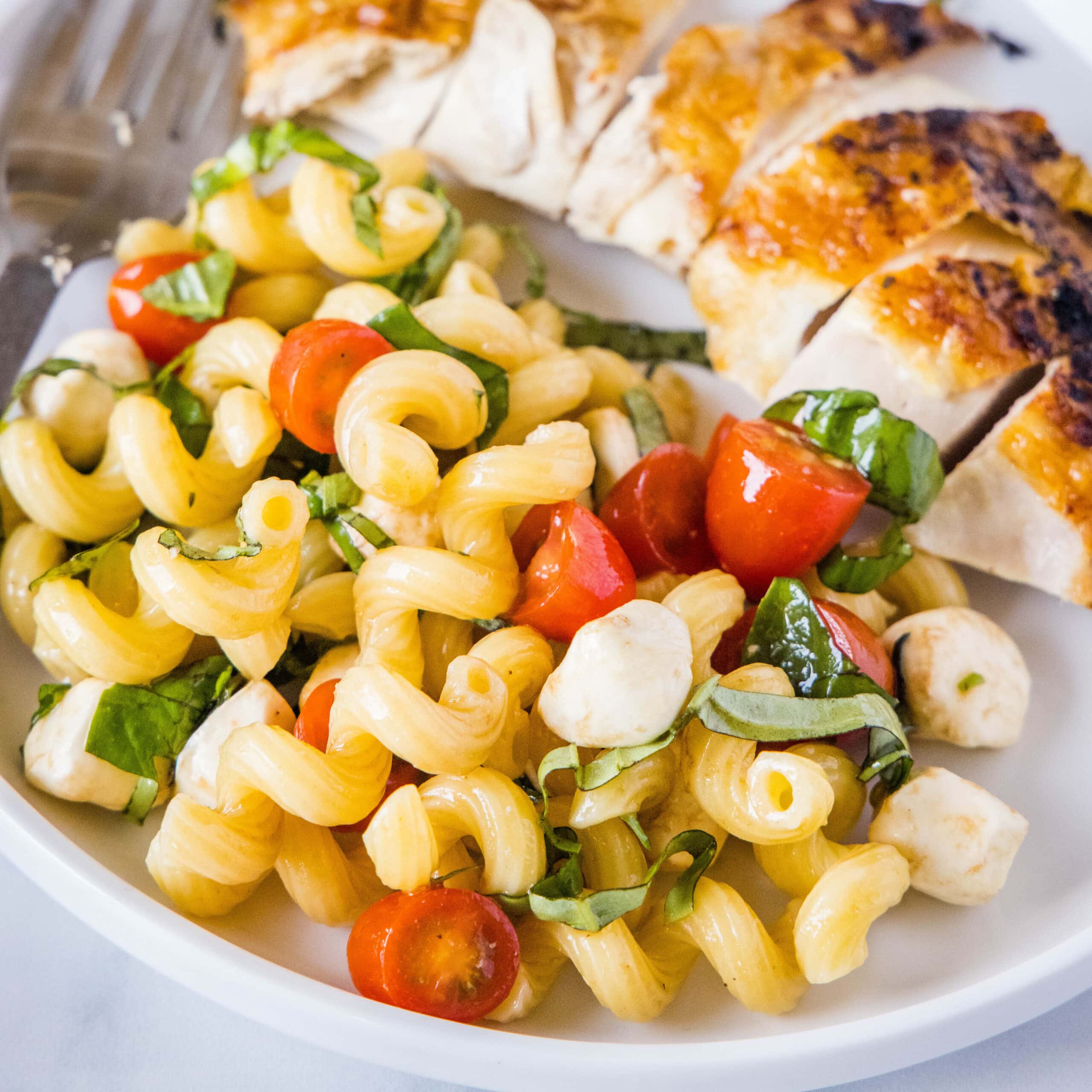 cropped in close up of pasta salad next to a piece of chicken