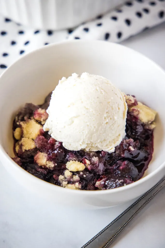 cherry cobbler in a white bowl with a scoop of ice cream on top