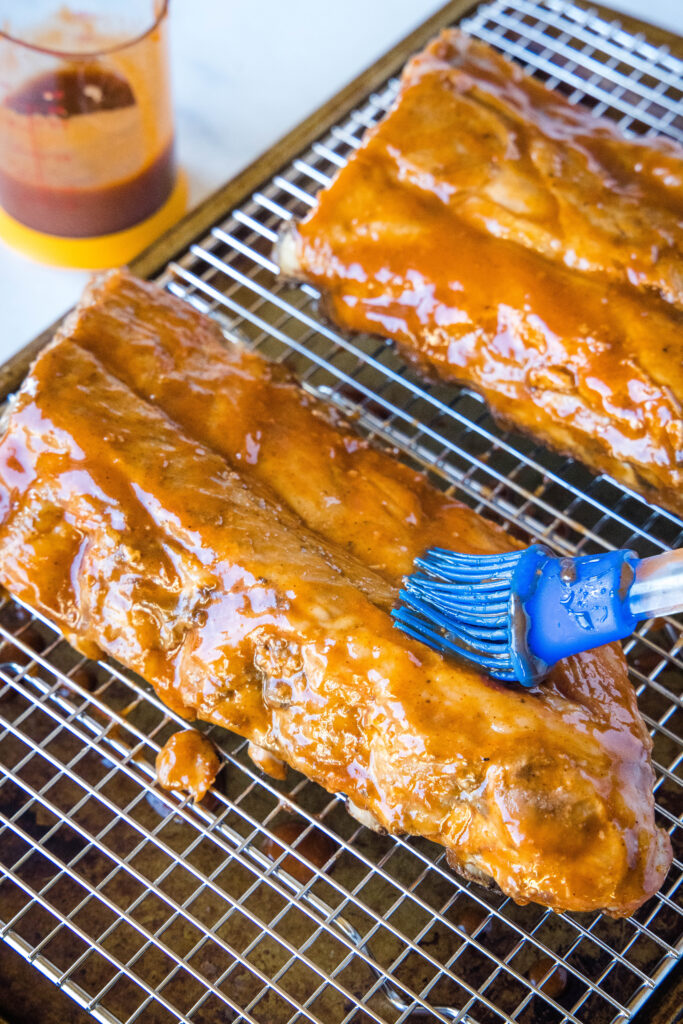 brushing sauce on ribs on a baking tray