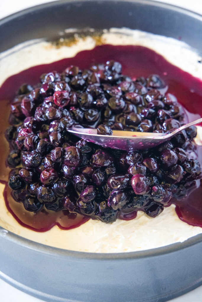 spreading blueberry filling over a cheesecake