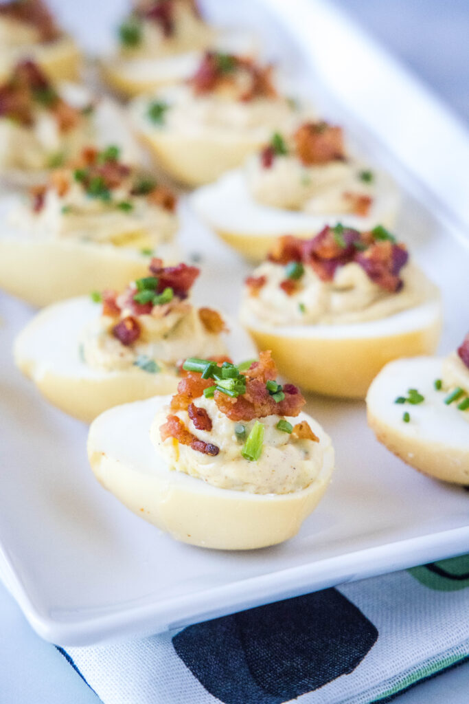 deviled eggs on a white plate topped with bacon and chives