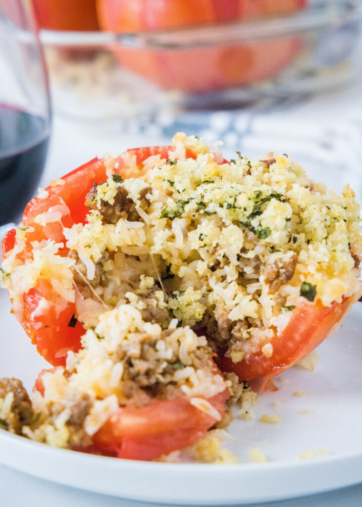 stuffed tomato on a white plate, cut open with rice and sausage