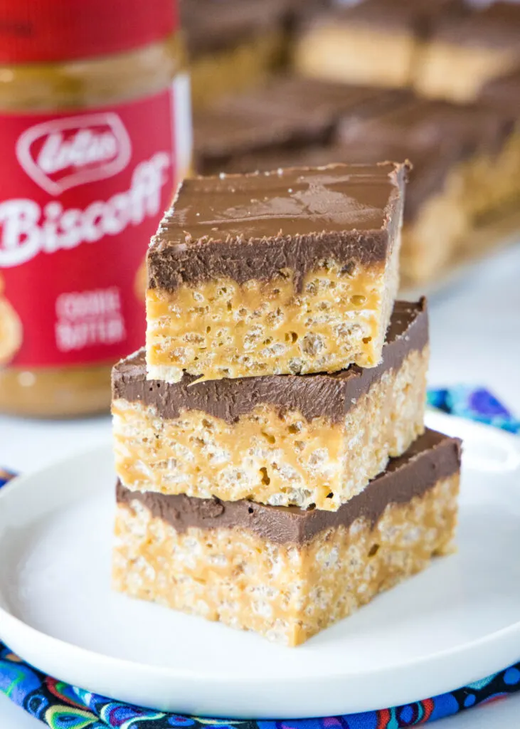 stacked  krispie treats on a white plate with jar of biscoff spread