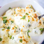close up scooping alfredo stuffed shells out of baking dish