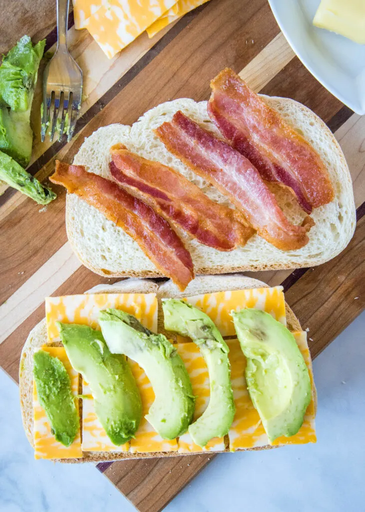 assembling sandwich with cheese and avocado and bacon on bread