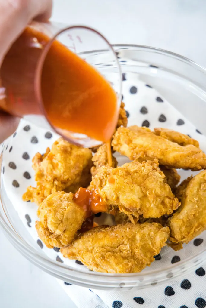 pouring sauce over breaded chicken pieces in a bowl