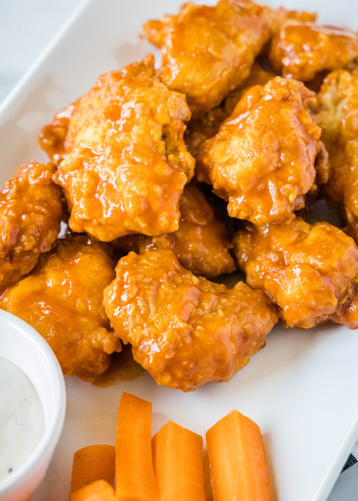 a plate of boneless buffalo wings with carrot sticks and ranch