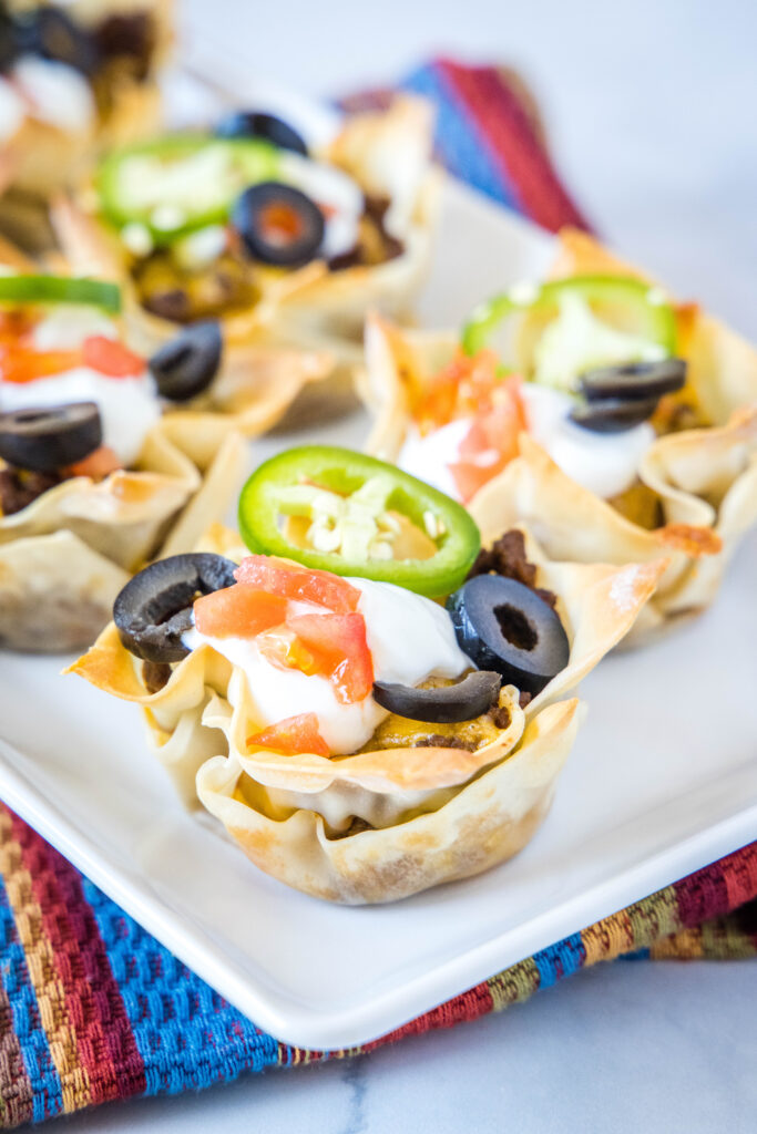 crispy taco cups arrange on a serving platter topped with sour cream and tomatoes