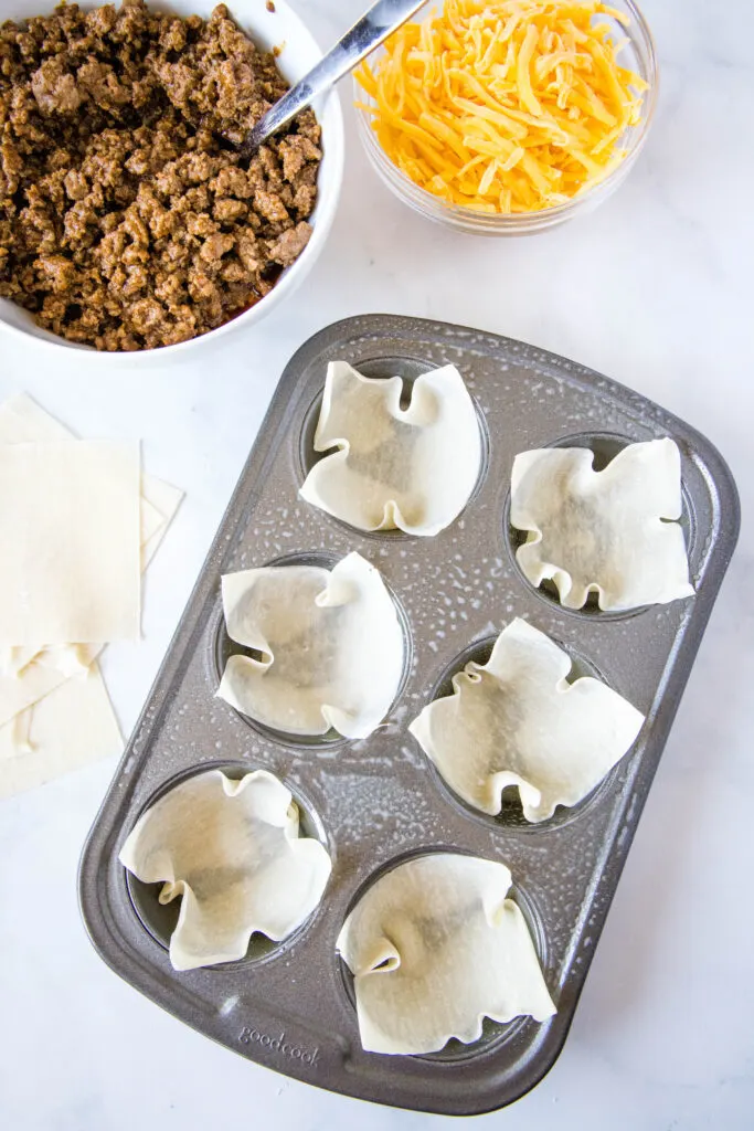 wonton wrappers in muffin tin with ground beef and cheese next to it