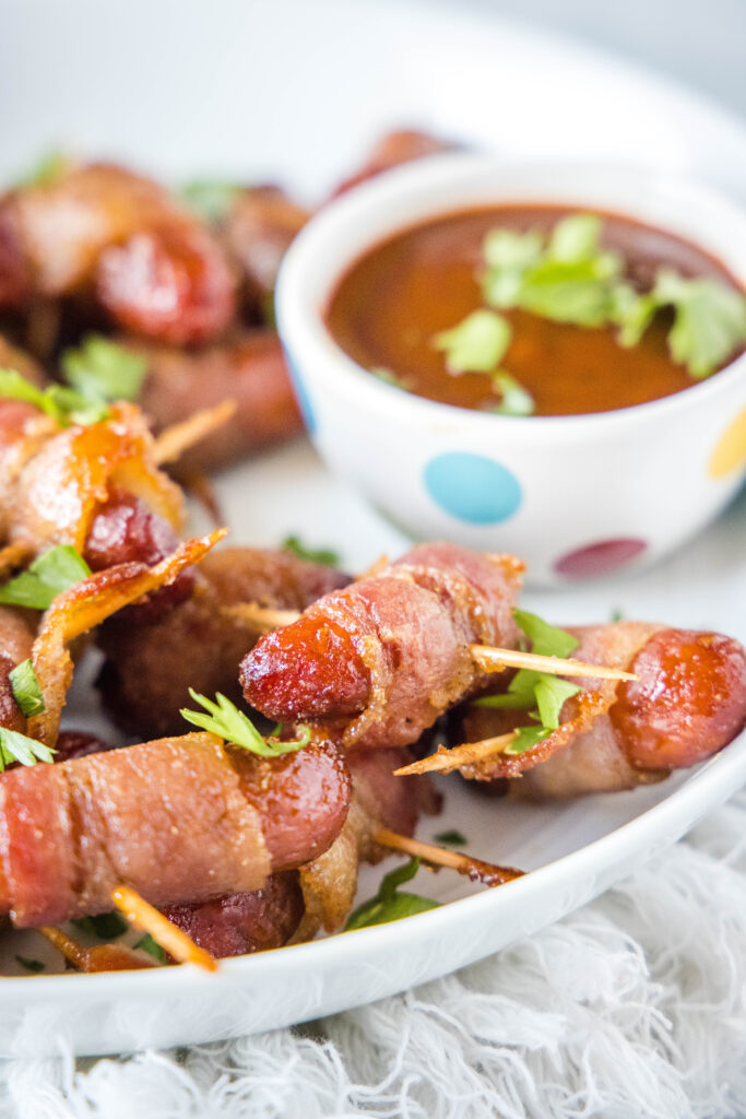 white tray with bacon wrapped smokies and a bowl of barbecue sauce