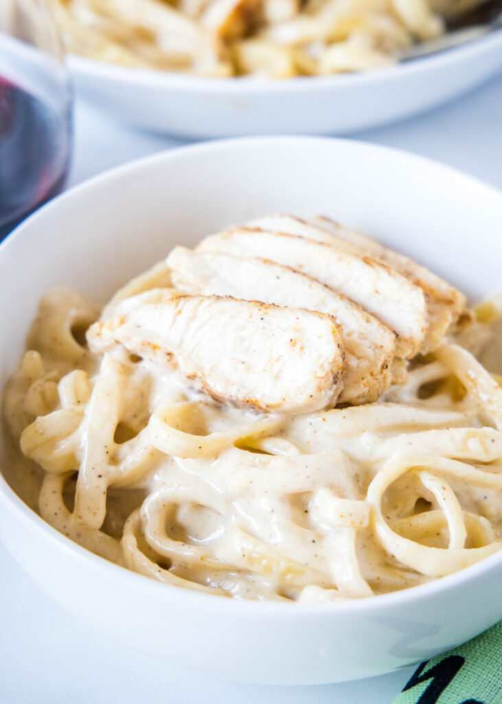 a while bowl with fettuccine alfredo with chicken on top