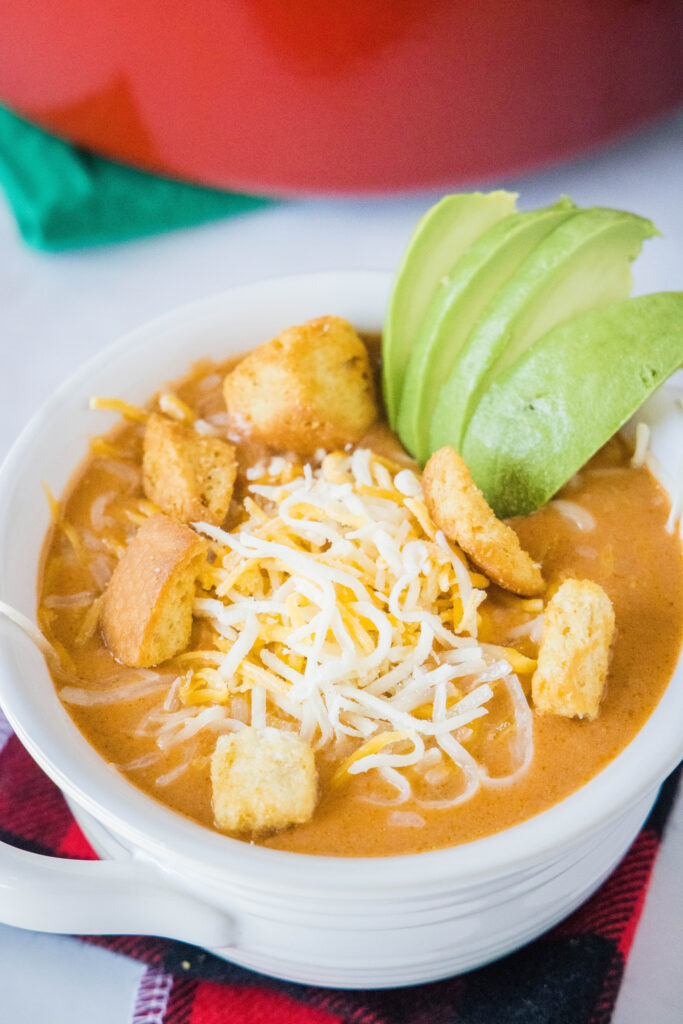 a bowl of soup topped with croutons, cheese, and avocado slices