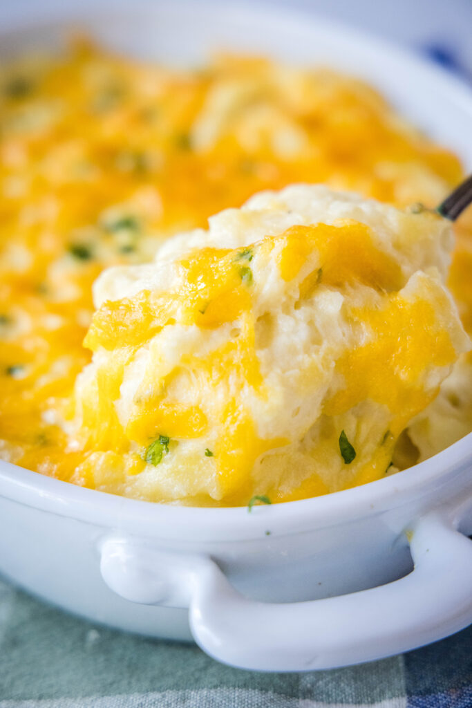 spooning out cheddar mashed potatoes from baking dish