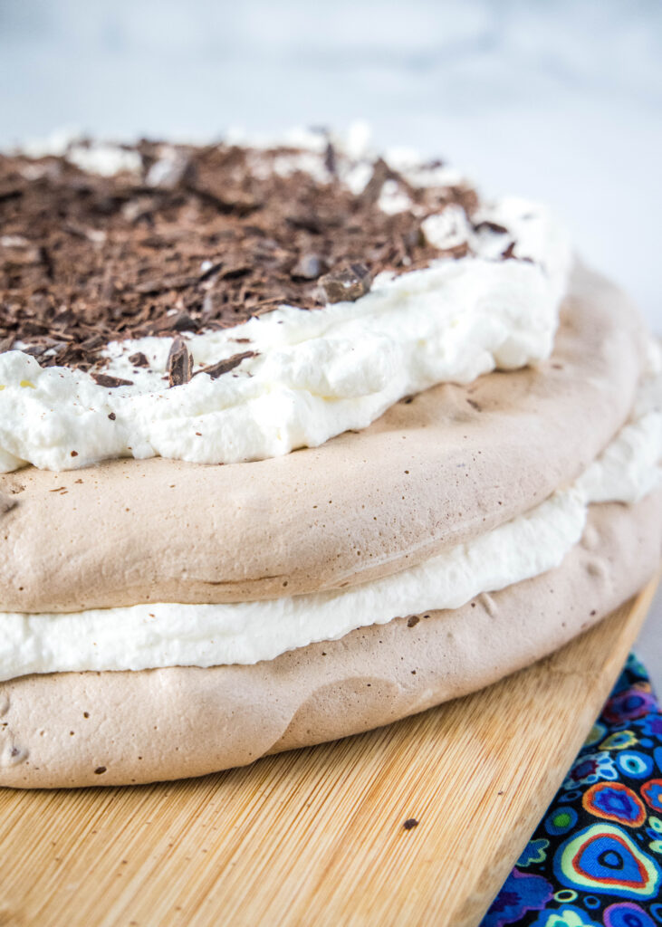 chocolate pavlova on a cutting board topped with whipped cream