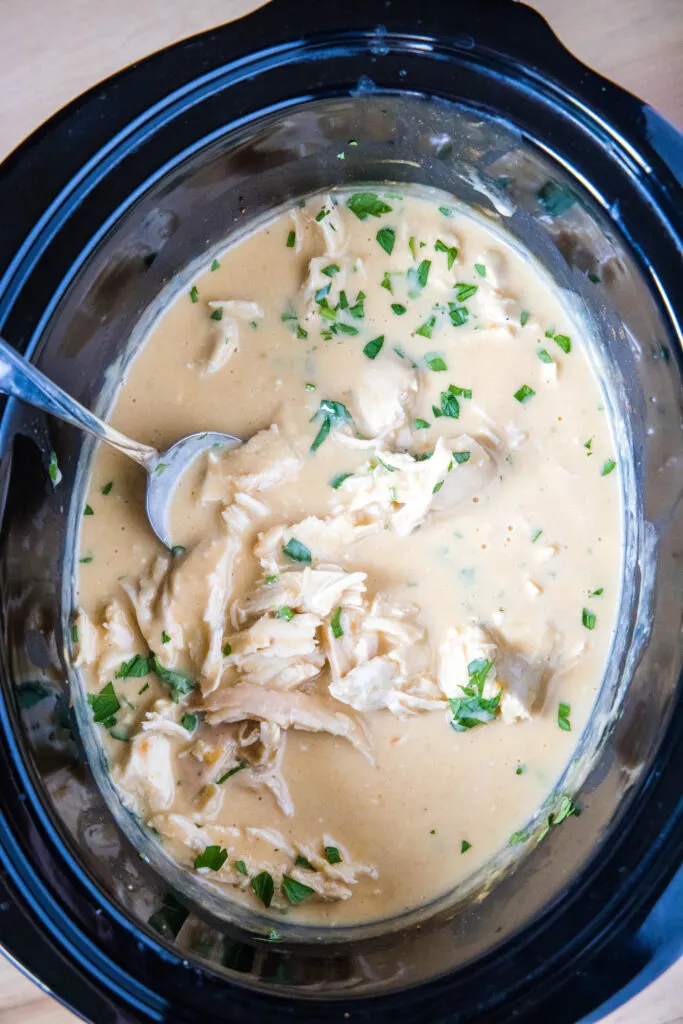 crockpot chicken and gravy in the slow cooker with a spoon