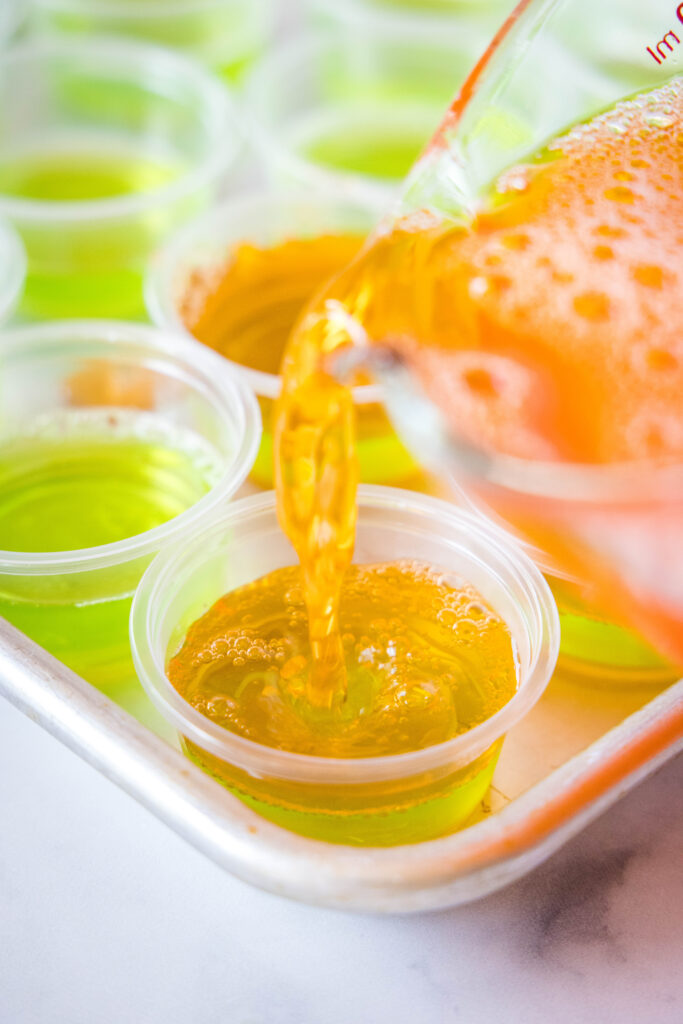 pouring orange jello over green in small cups