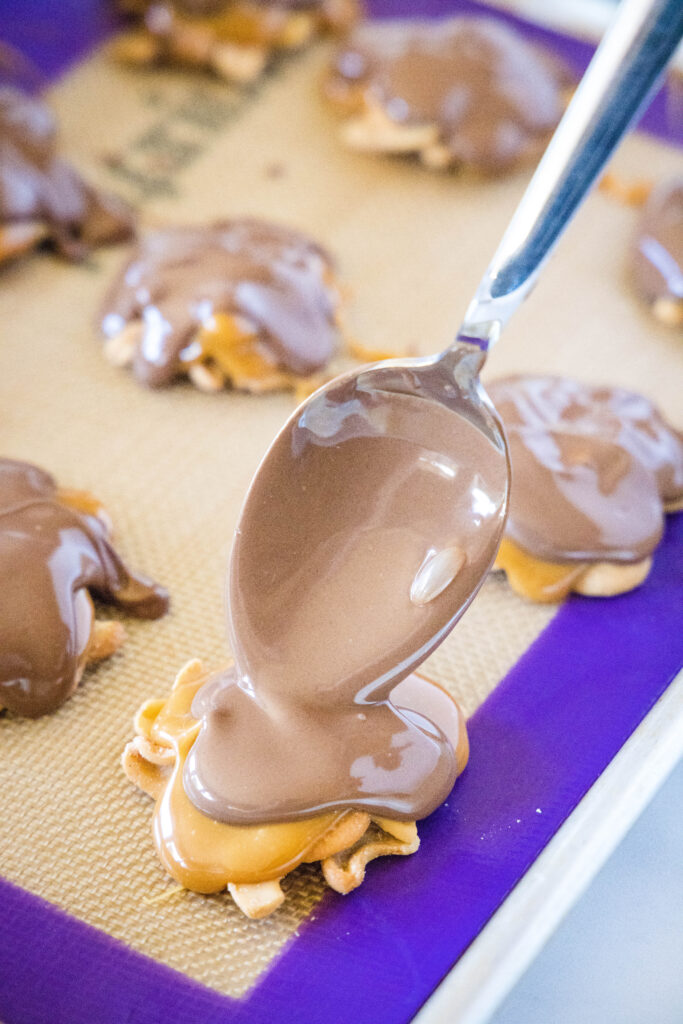 spoon melted chocolate over caramel cashew clusters