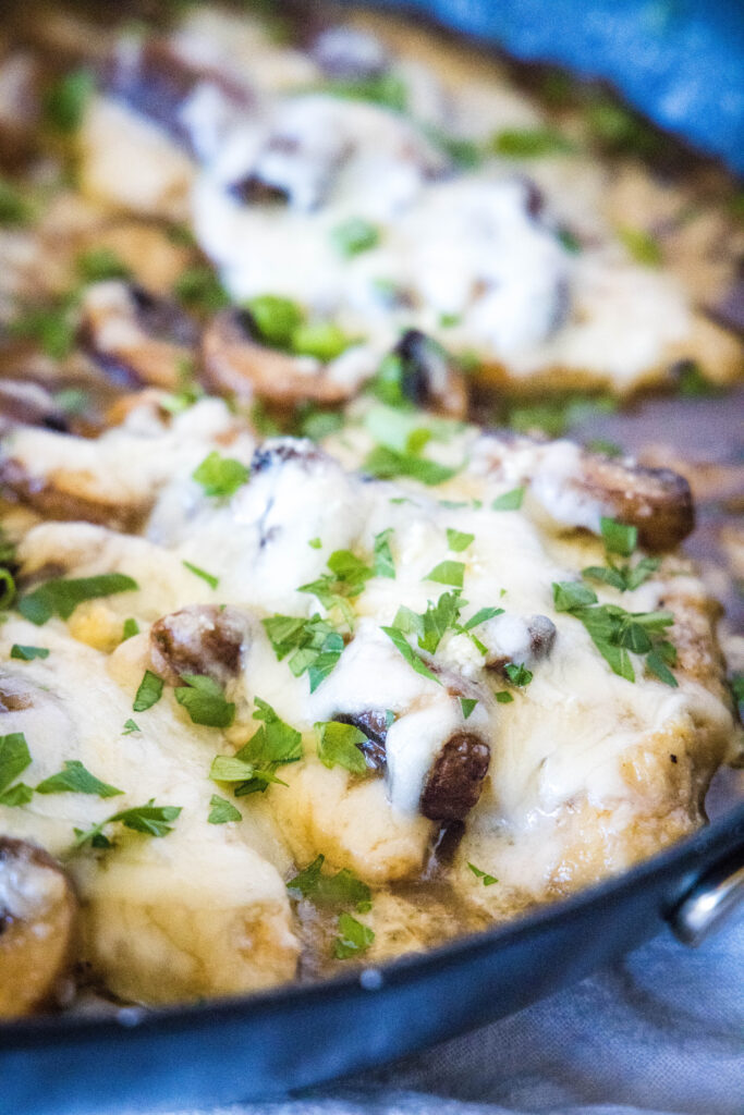 chicken with melted cheese and parsley in a skillet