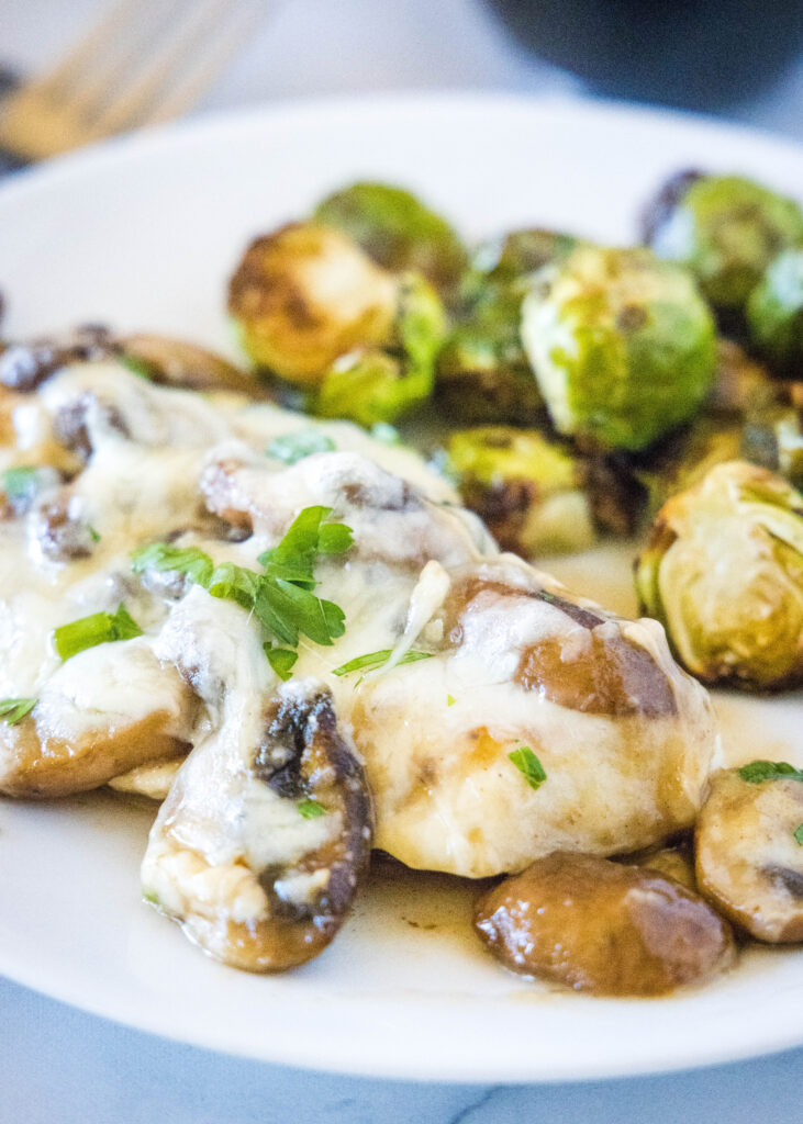 chicken with mushrooms and cheese on a white plate with brussel sprouts