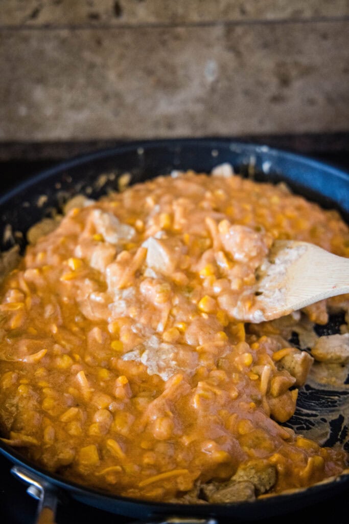 adding corn and cheese sauce to the cooked chicken in a skillet