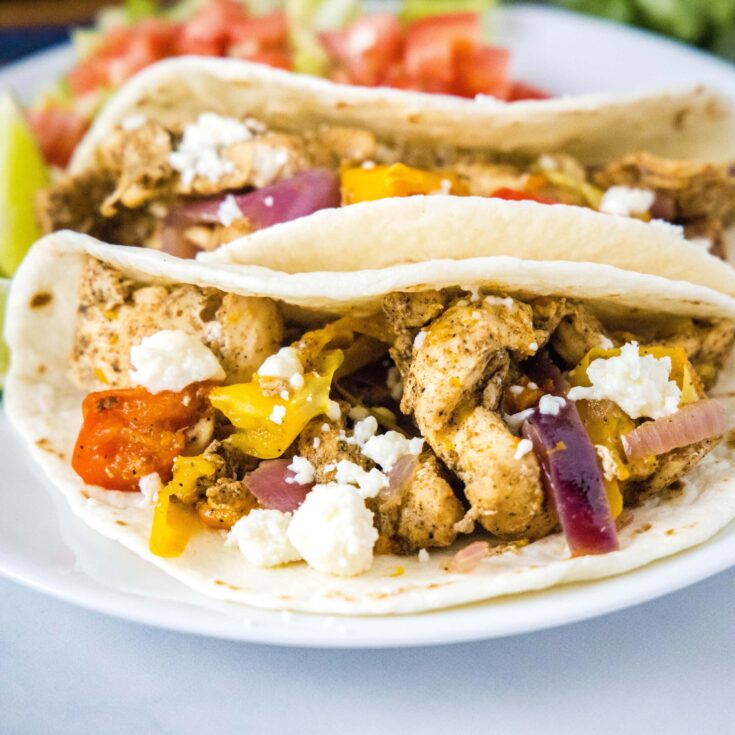 close up square image of chicken fajitas on a white plate