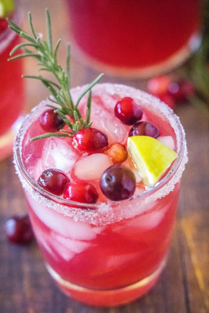 looking down on a glass with ice , cranberries, and a rosemary sprig