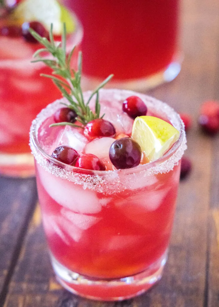 cranberry margarita in a glass with cranberries and a sprig of rosemary