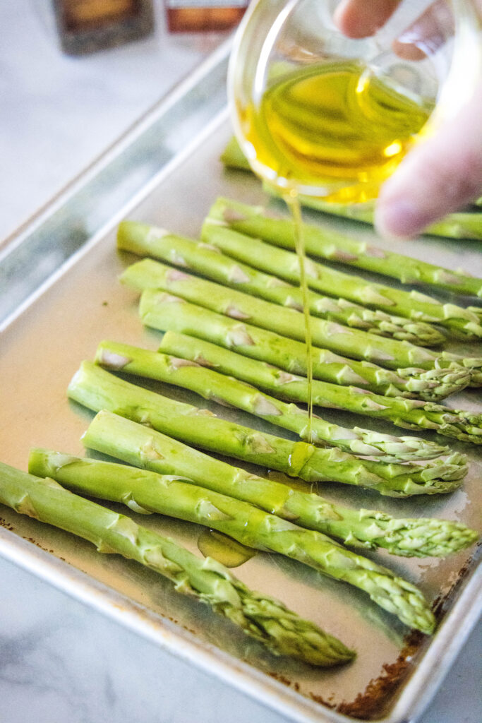 drizzling olive oil over a tray of asparagus