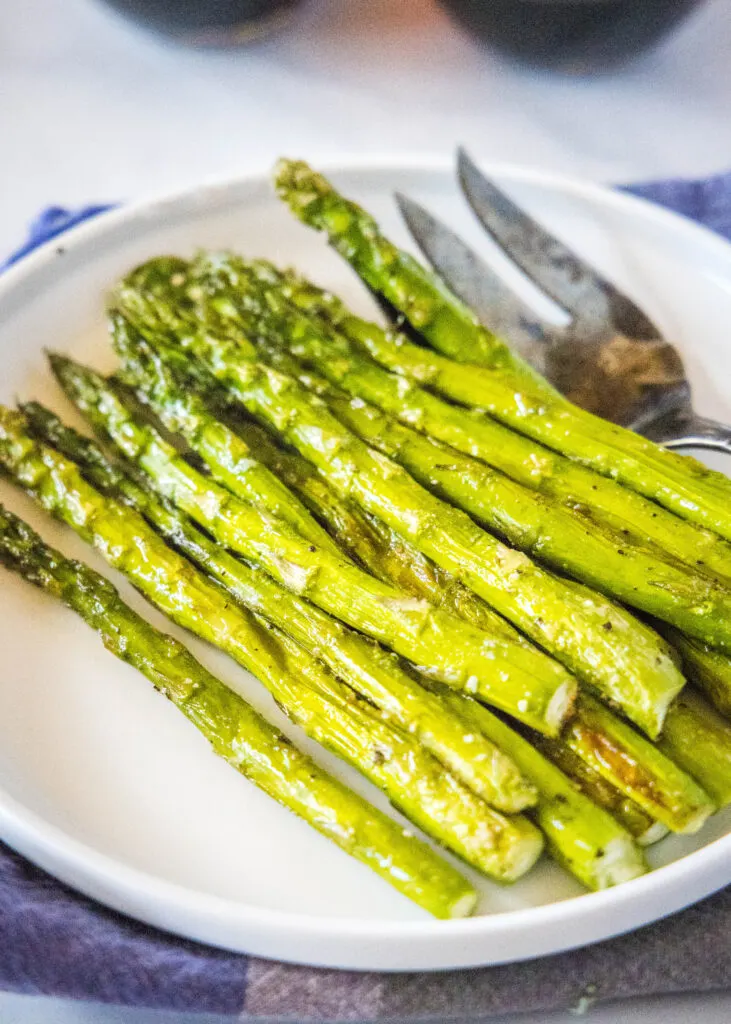 roasted asparagus on a white plate with serving fork