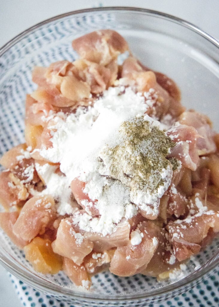 adding cornstarch, salt and pepper to chicken in a mixing bowl