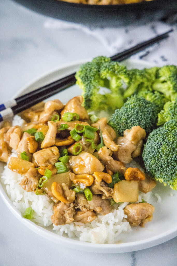 Cashew chicken over rice with broccoli on a white plate