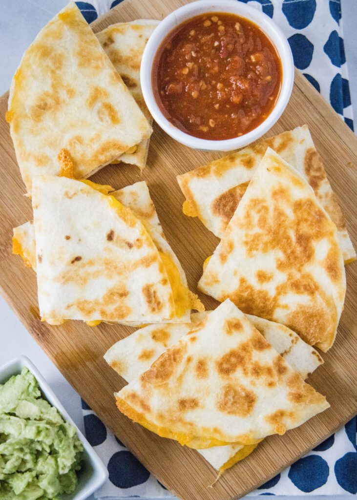 slices of cheese quesadilla on a cutting board with salsa and guacamole