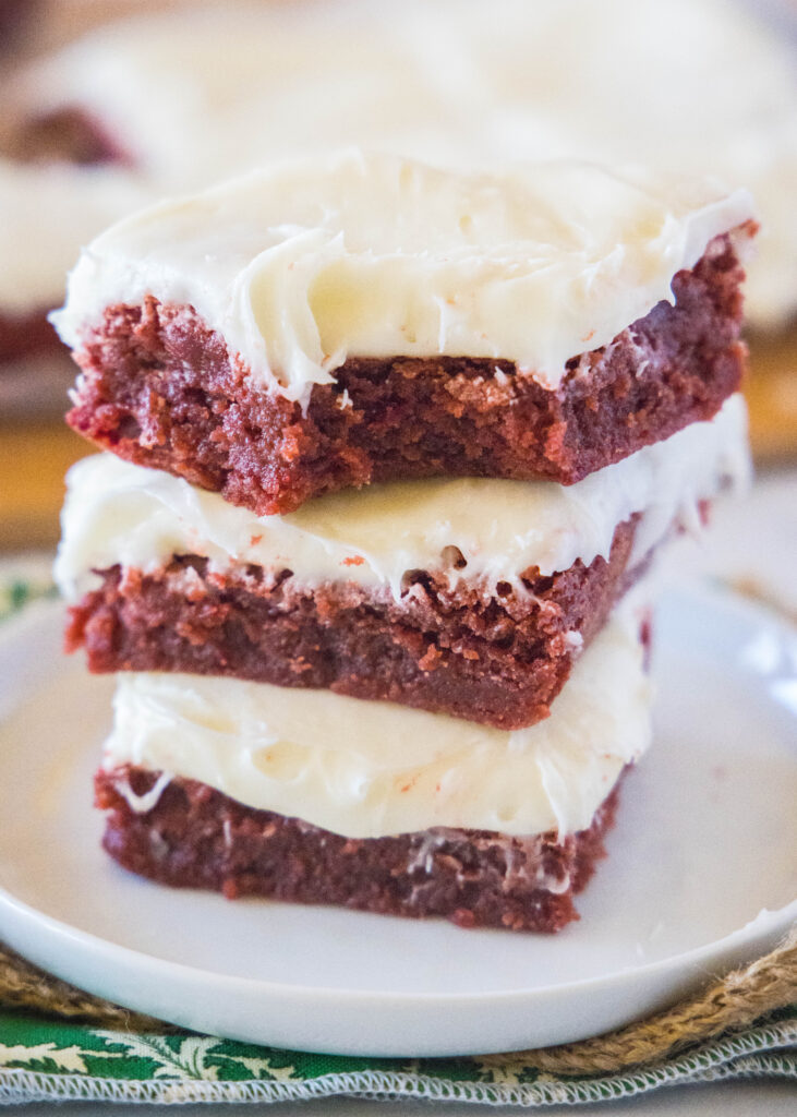 red velvet brownies stacked on a white plate with a bite taken out of one