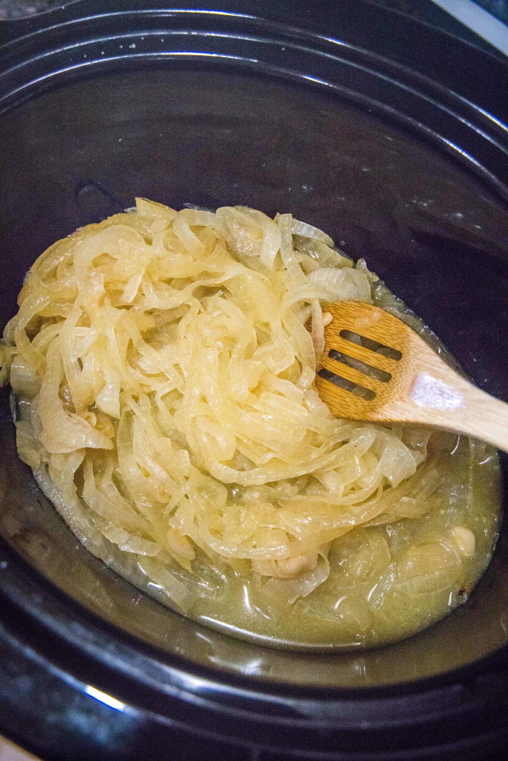 cooked onions in a crockpot with a wooden spoon