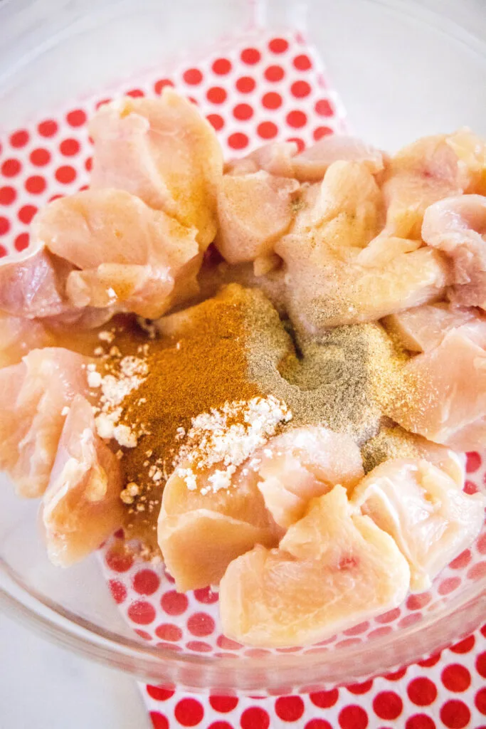 chicken pieces in a bowl with seasoning sprinkled over the top