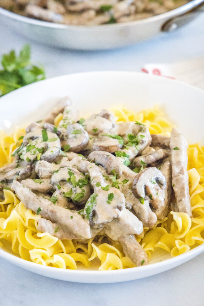 white plate with beef stroganoff over egg noodles