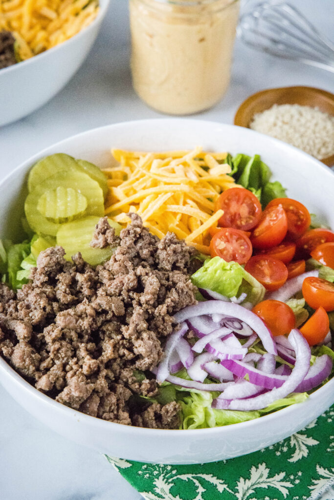 Bowl with a salad in it, garnished with beef, pickles, onions, cheese, tomatoes